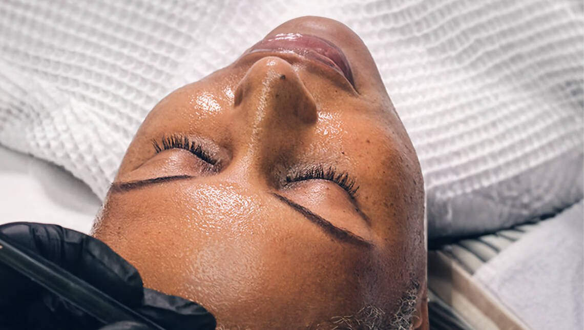 En kvinder ligger afslappet med lukkede øjne og får en ansigtsbehandling.